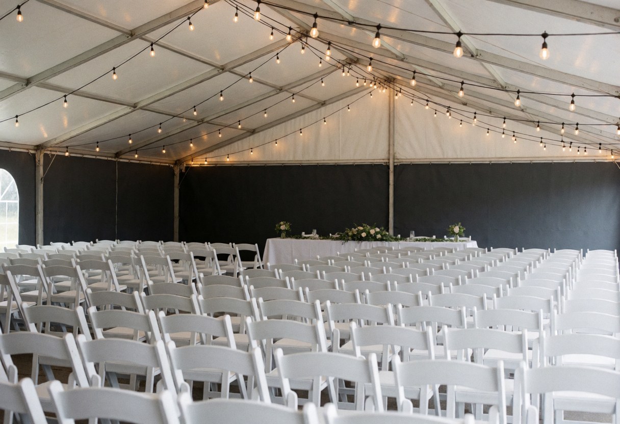 Interior view of an event furniture rental space featuring white chairs, a decorated table, and hanging lights ready for setup.