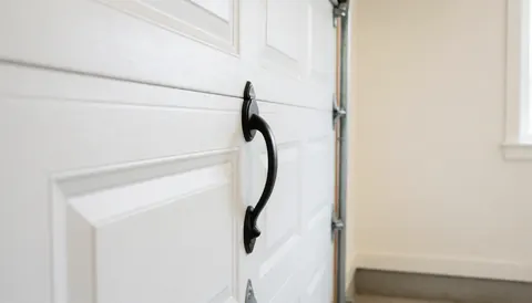 Close-up of a white residential garage door featuring a sleek black handle against a clean, light-colored wall background.