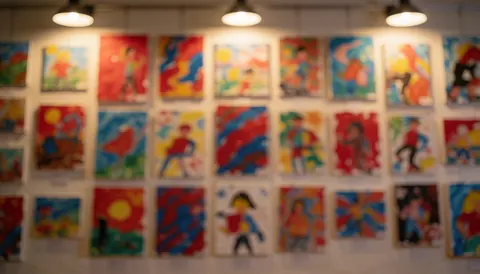 Gallery background featuring multiple abstract children's paintings in frames, illuminated by warm lights, ideal for text overlay.