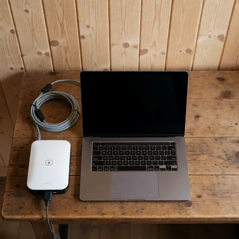 A laptop and satellite modem connected on a rustic wooden table, suitable for mountain hut internet service.