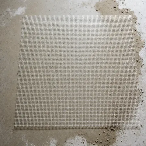 White fiberglass mesh laid over gray concrete floor with dust particles, prepared for cork flooring installation
