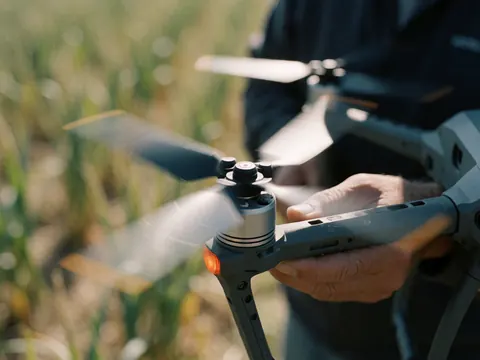 Close-up view of adult hands holding a drone with spinning propellers in an agricultural field, highlighting precision and technology for aerial photography services.