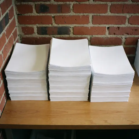 Three neat stacks of white paper arranged on a wooden table with a red brick wall background and natural lighting.