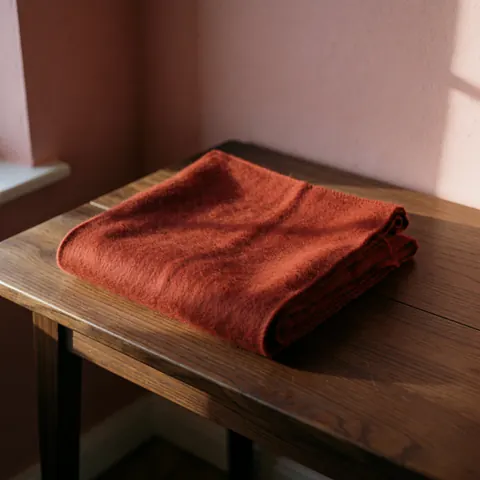 Folded red alpaca scarf resting on a dark wooden table with pink walls and natural light