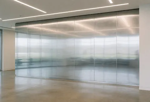 Polished metal office wall reflecting linear ceiling lights and polished concrete floor in a clean corporate interior.