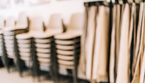 Stacked chairs and fabric swatches on a blurred warm-toned background, ideal for text overlay in event furniture rental contexts.