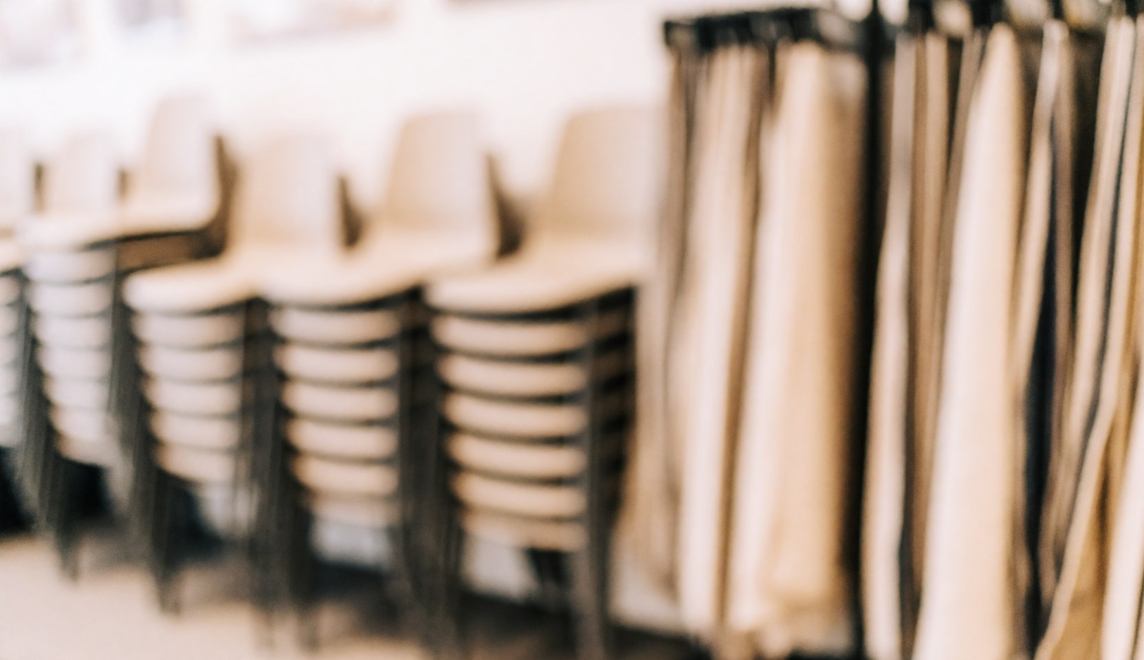 Stacked chairs and fabric swatches on a blurred warm-toned background, ideal for text overlay in event furniture rental contexts.