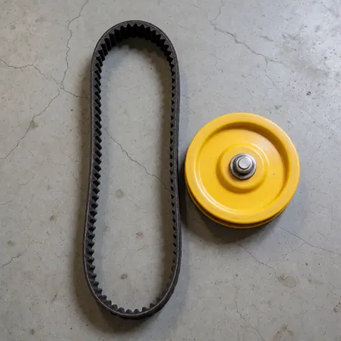 Close-up of a black toothed drive belt and a yellow pulley resting on a concrete floor, suitable for appliance repair parts.
