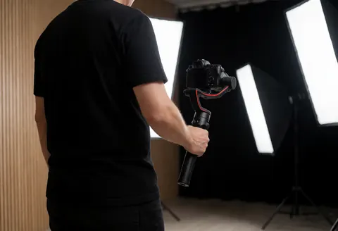 Professional photographer holding a camera with a gimbal stabilizer in a studio setting with softbox lighting and wooden background.