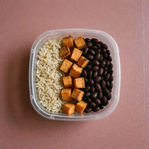 Top view of a healthy food container filled with rice sweet potato and beans on a pink background