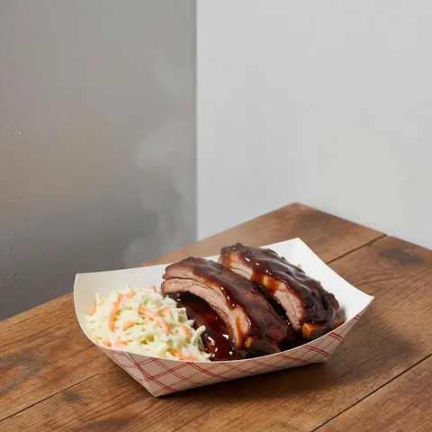 Steaming barbecue ribs with coleslaw served in a paper container on a wooden table