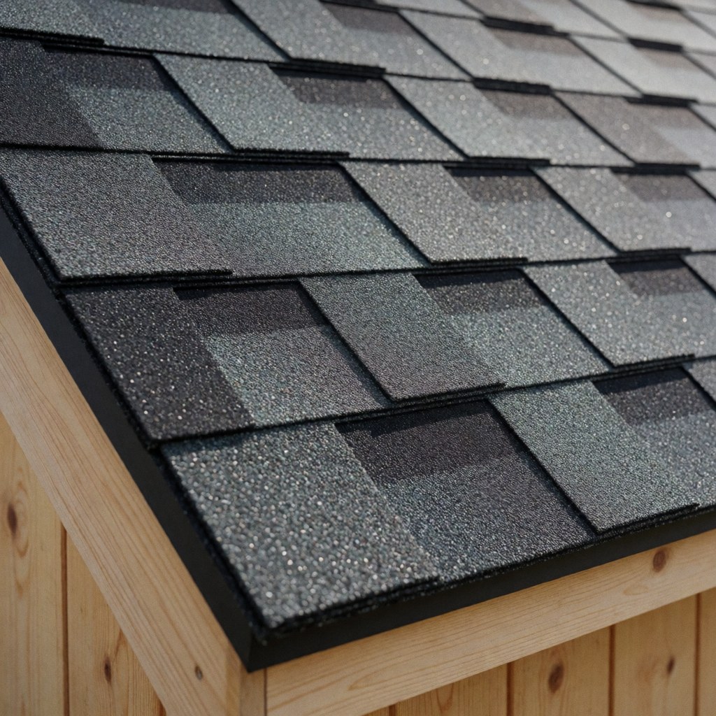 Close-up view of dark gray granular asphalt shingles installed on a sloped roof above light wood walls under sunlight