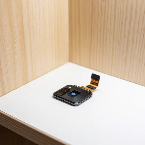 Phone camera module with sensor and flex cable on white surface with light wood walls and professional lighting