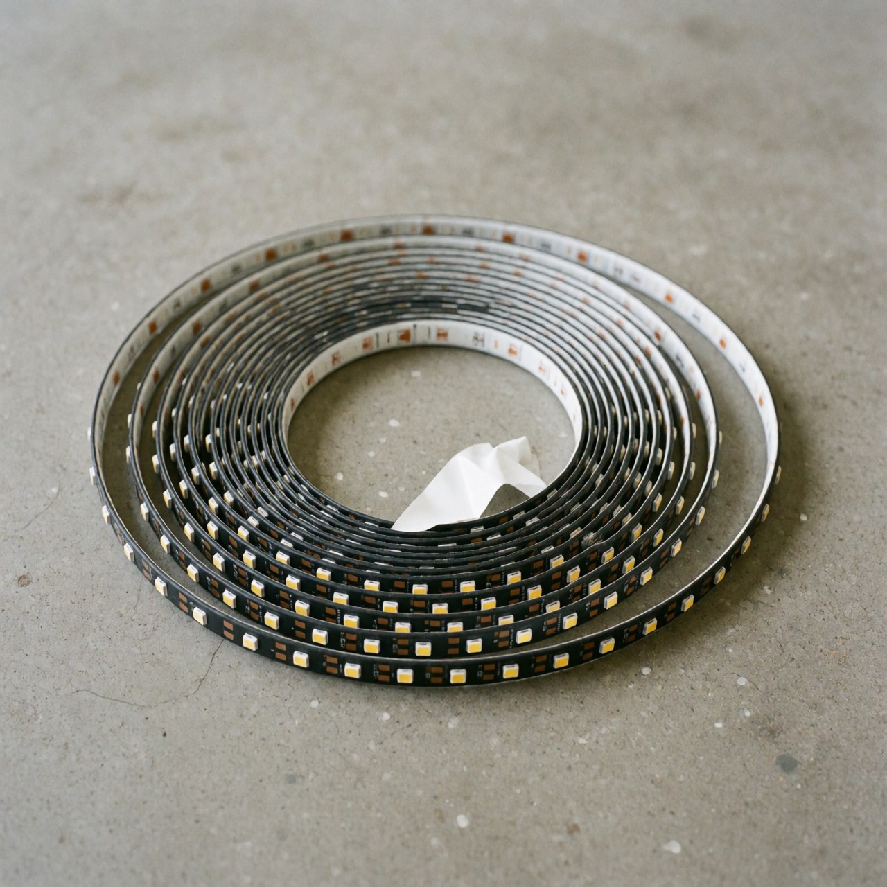 Rolled flexible adhesive LED strip resting on a gray concrete floor, suitable for event lighting and decoration.