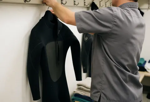 Aquarium employee hanging a black wetsuit on a metal hook with folded towels in the background and white walls.