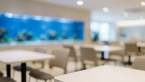 Blurred tables and chairs in a bright airy coffee shop interior featuring a blue aquarium tank on the wall, ideal text background
