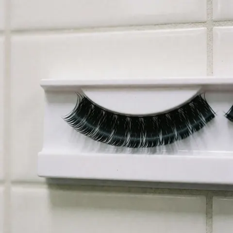 Black voluminous false tears displayed on a white stand against a white tiled wall with soft diffuse lighting