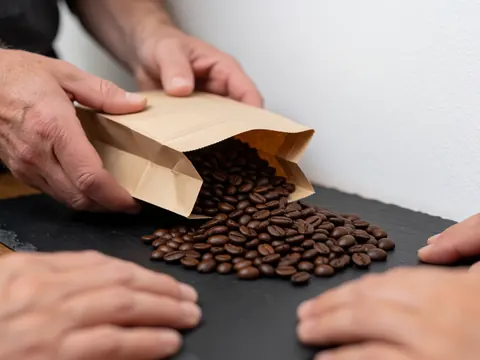 Dark roasted coffee beans being poured from a brown paper bag onto a dark stone surface, highlighting the rich texture of the beans.
