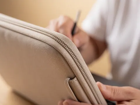 Detailed view of a metal zipper and beige fabric stitching on a computer case, highlighting texture and craftsmanship.