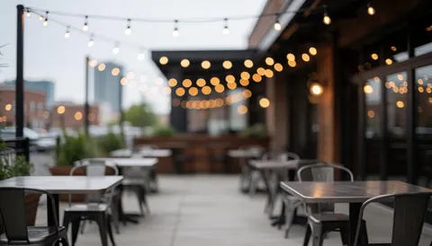 Outdoor terrace with metal tables and chairs, hanging lights, and a blurred city background suitable for commercial text