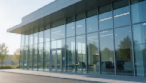 Exterior view of a modern commercial building featuring large glass windows, illuminated by morning light with blue and gray tones.