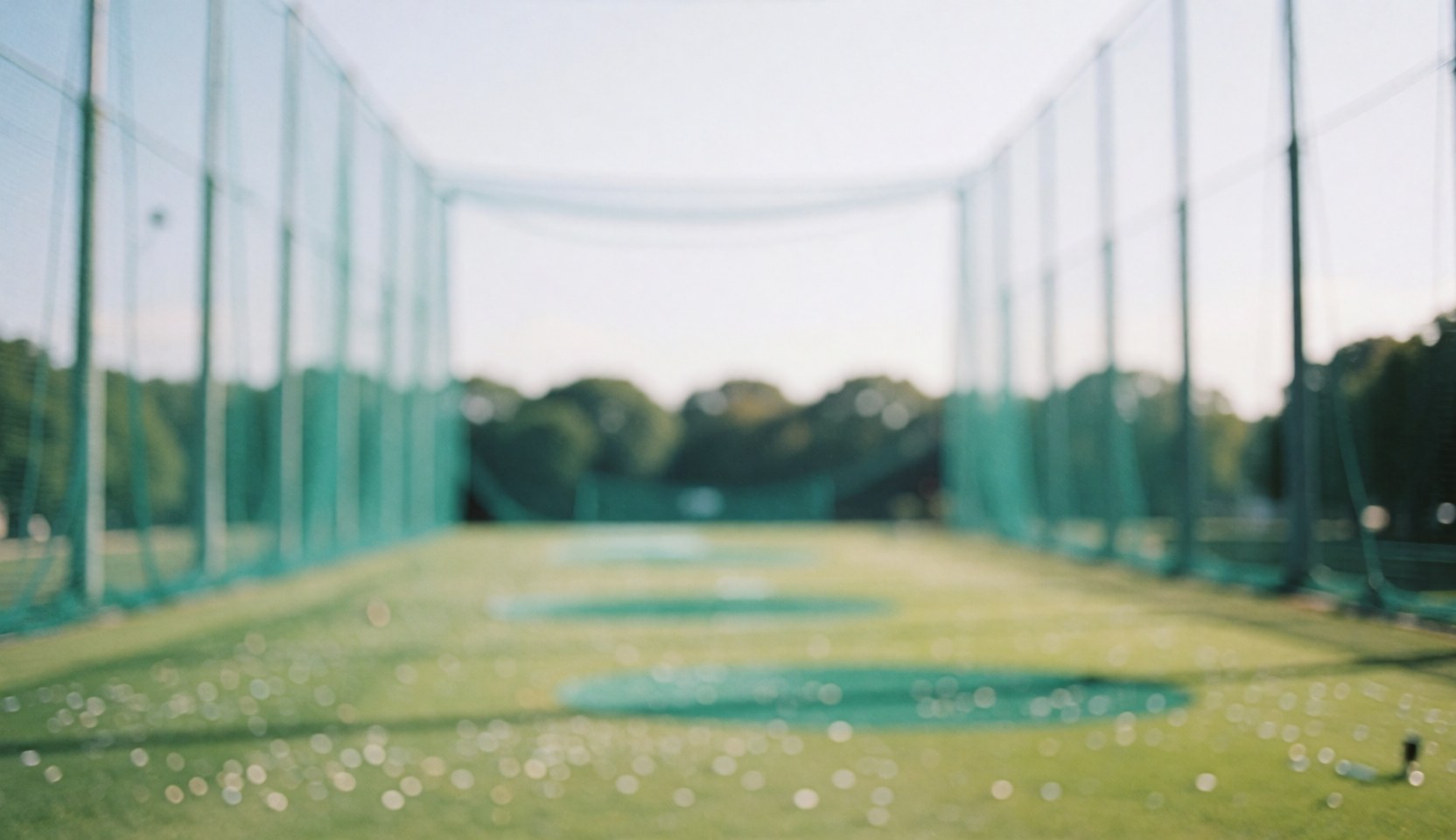 Soft-focus background of a golf driving range with a green net, grass, and distant trees, providing a bright and uniform surface ideal for text overlay.