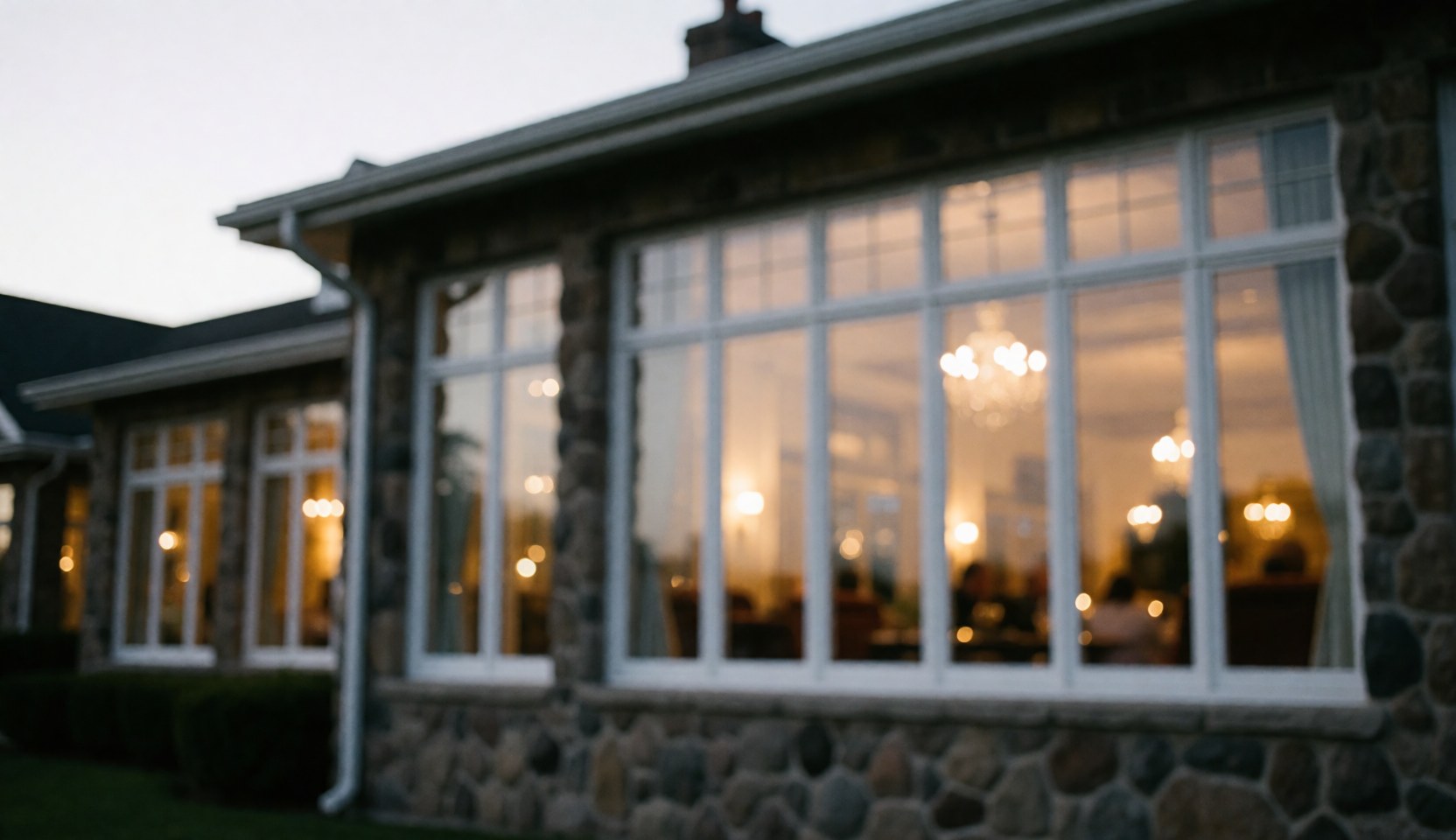 Stone facade of a golf club building featuring large windows that reveal warm interior lighting and a cozy evening atmosphere.
