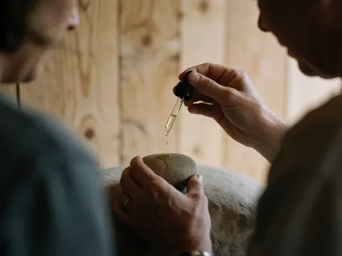 Essential oil drops falling on a stone with hands working against a wooden background creating a relaxing spa scene