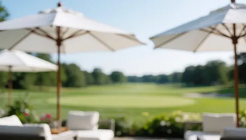 White umbrellas on a golf course terrace with blurred green grass, ideal for text and outdoor events