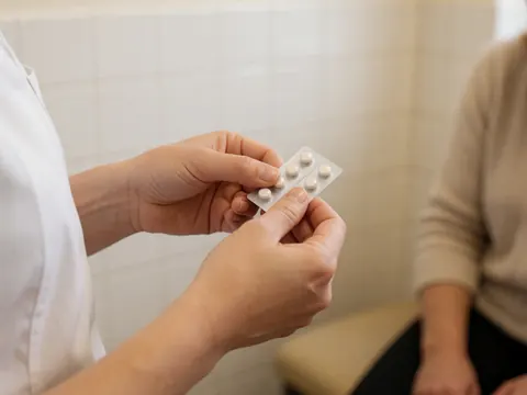 Close-up of hands opening a blister pack of sublingual tablets in a clinical setting with white tiled walls.