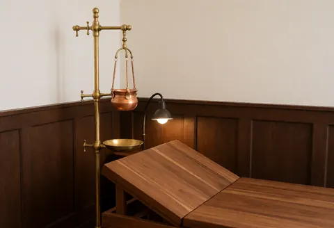 Ayurvedic Shirodhara massage setup with bronze stand and wooden table in a corner with dark wood walls and warm lighting