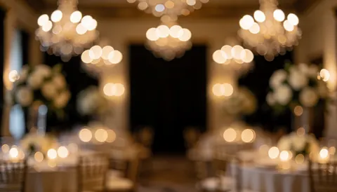 Blurred background of a wedding reception featuring warm chandelier and candle lights, tables, and floral arrangements, ideal for text overlay.