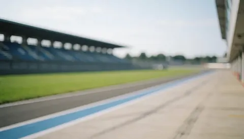 Blurred race track background with green grass, empty grandstands, and blue lines, ideal for text overlays and business announcements.