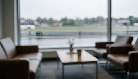 Brown sofas and coffee table in a waiting room with a window overlooking a race track in the rain