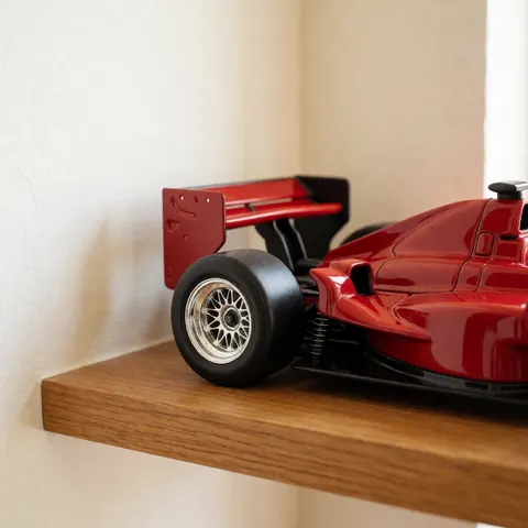 Red race car model with visible suspension details and rear wing resting on a wooden shelf in soft natural light