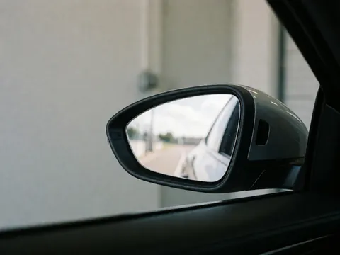 Close-up of a car side mirror reflecting a road, sky, and background walls in a clean realistic image