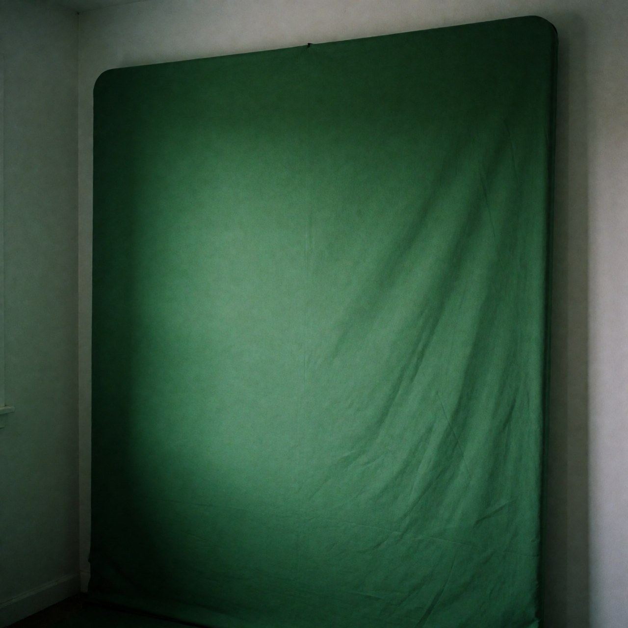 Green screen background for professional photography, ideal for digital composition, with soft lighting and white walls in a studio.