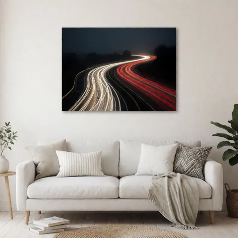 Artistic long exposure photo showing red and white car light trails on a curved road under a dark sky, displayed as wall decor in a home interior