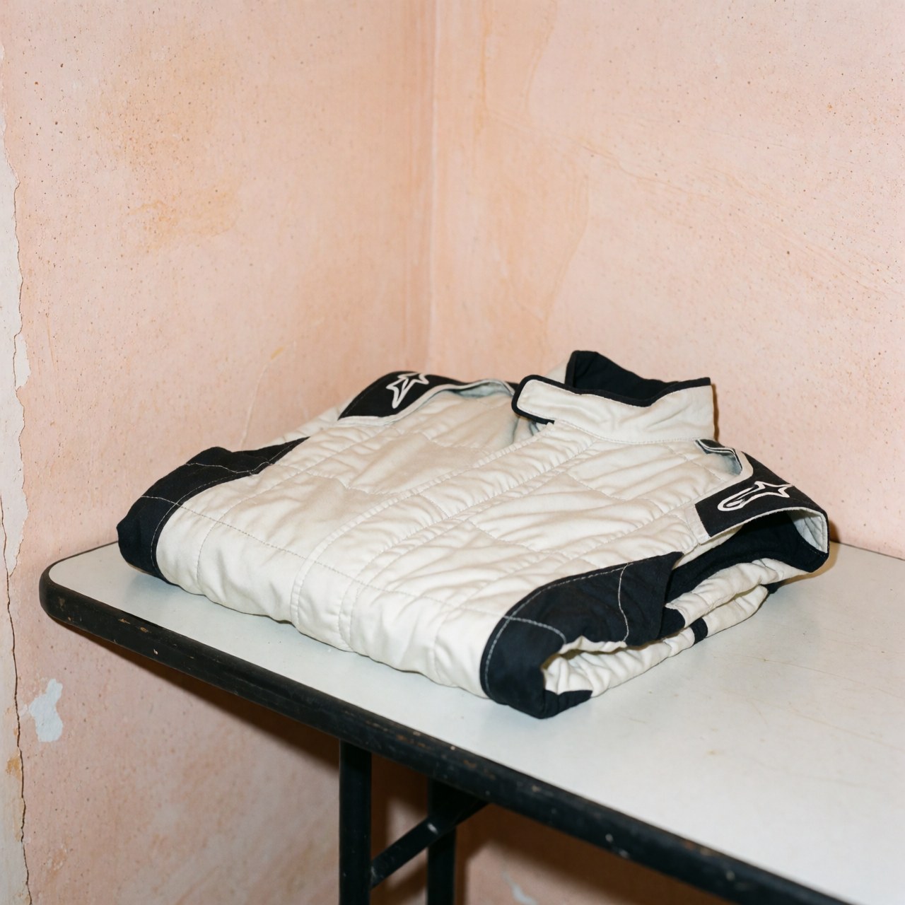 Folded black and white racing jacket on white table with terracotta walls and visible texture