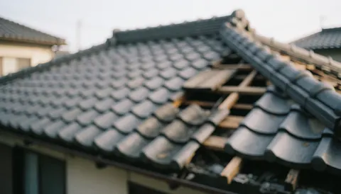 Close-up view of a residential roof damaged by a storm showing missing shingles and exposed wooden structure against a blurred background suitable for text overlay