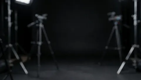 Dark studio background with blurred tripods and lights, ideal for text, professional and calm atmosphere