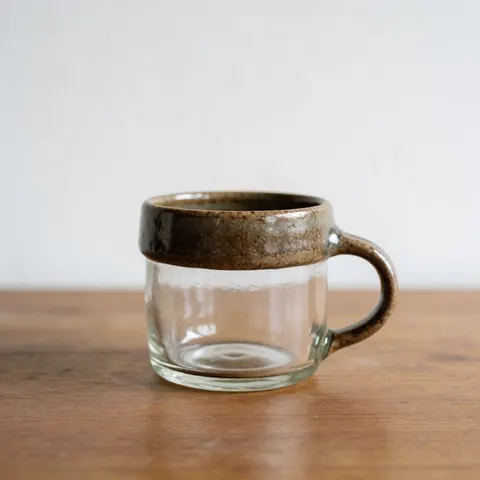 A textured glass mug with a rustic rim sits on a wooden table against a white background, showcasing artisanal glassblowing craftsmanship.