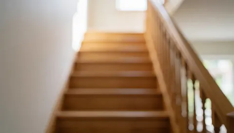 A wooden staircase with a railing set against a blurred background with natural light, suitable for commercial text overlays.