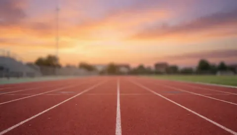 Empty athletic track with white lines against an orange and purple sunset sky, serving as a background for sports training text