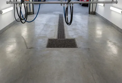 Close-up of a metal faucet fixture installed in a car wash bay with concrete flooring and fluorescent lighting overhead