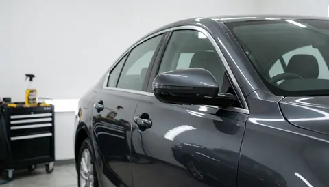 A glossy gray vehicle inside a car wash facility with bright overhead lights reflecting off the surface and a tool cart nearby