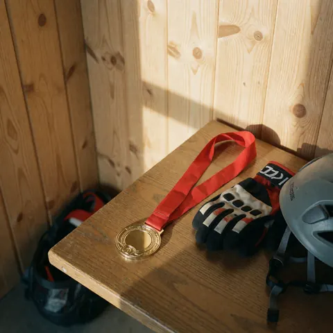 Gold medal with red ribbon, climbing gloves, and helmet on wooden table with wood panel walls