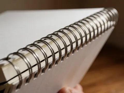 Close-up detail of a white notebook metal clasp with paper texture and warm wooden background