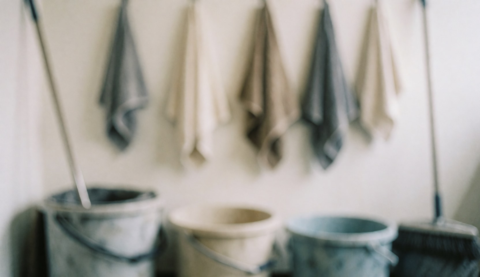 Blurred background of a cleaning area with metal buckets and hanging towels in neutral tones, ideal for motorcycle repair services.