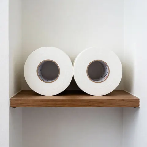 Two clean new rolls of white athletic tape placed on a wooden shelf against a white wall with bright uniform lighting